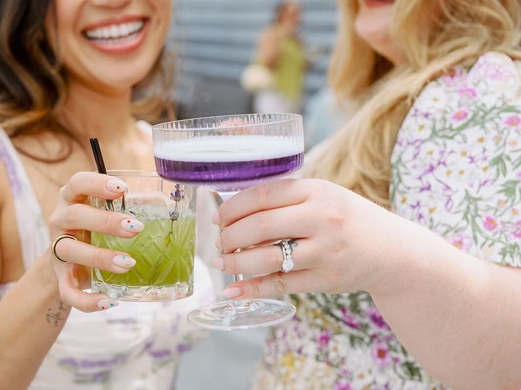 Women with colorful drinks performing a toast in a whimsical garden rooftop