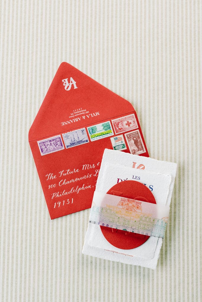 custom wedding invitation stacked next to a wedding invitation envelope with calligraphy and vintage stamps