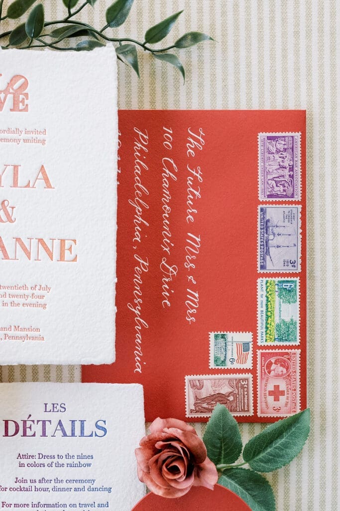 white ink calligraphy on red wedding invitation envelopes styled with vintage stamps